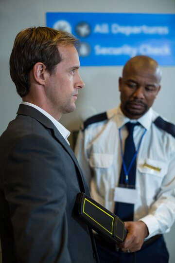 airport-security-officer-using-hand-held-metal-detector-check-commuter_107420-95856